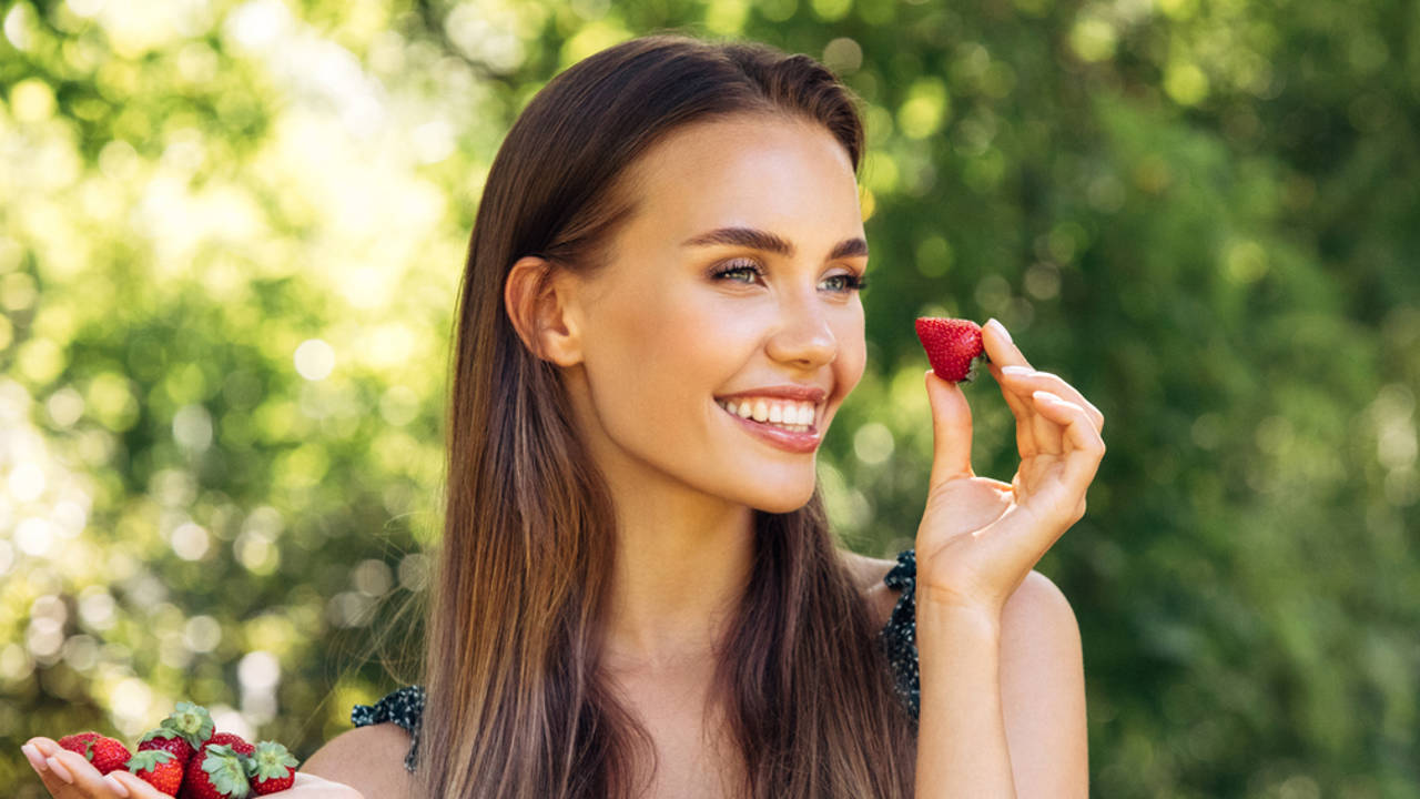 mujer joven sonriendo comiendo fresas