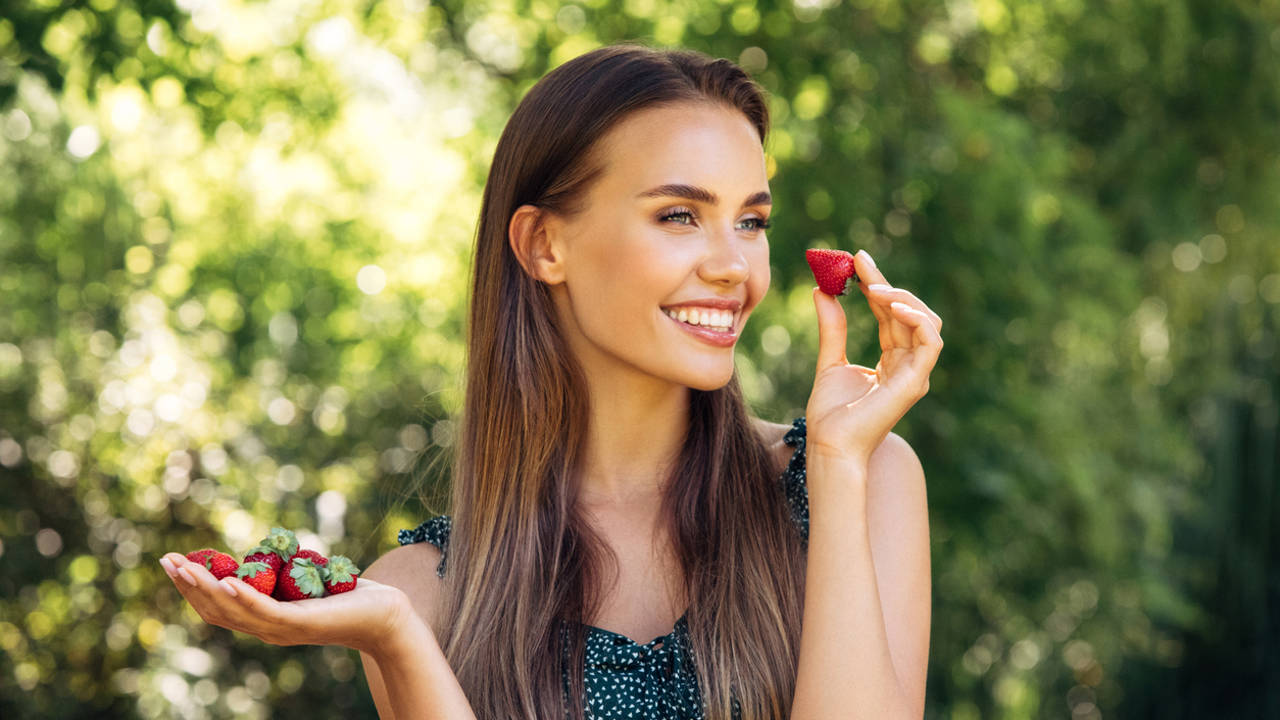 mujer joven sonriendo comiendo fresas