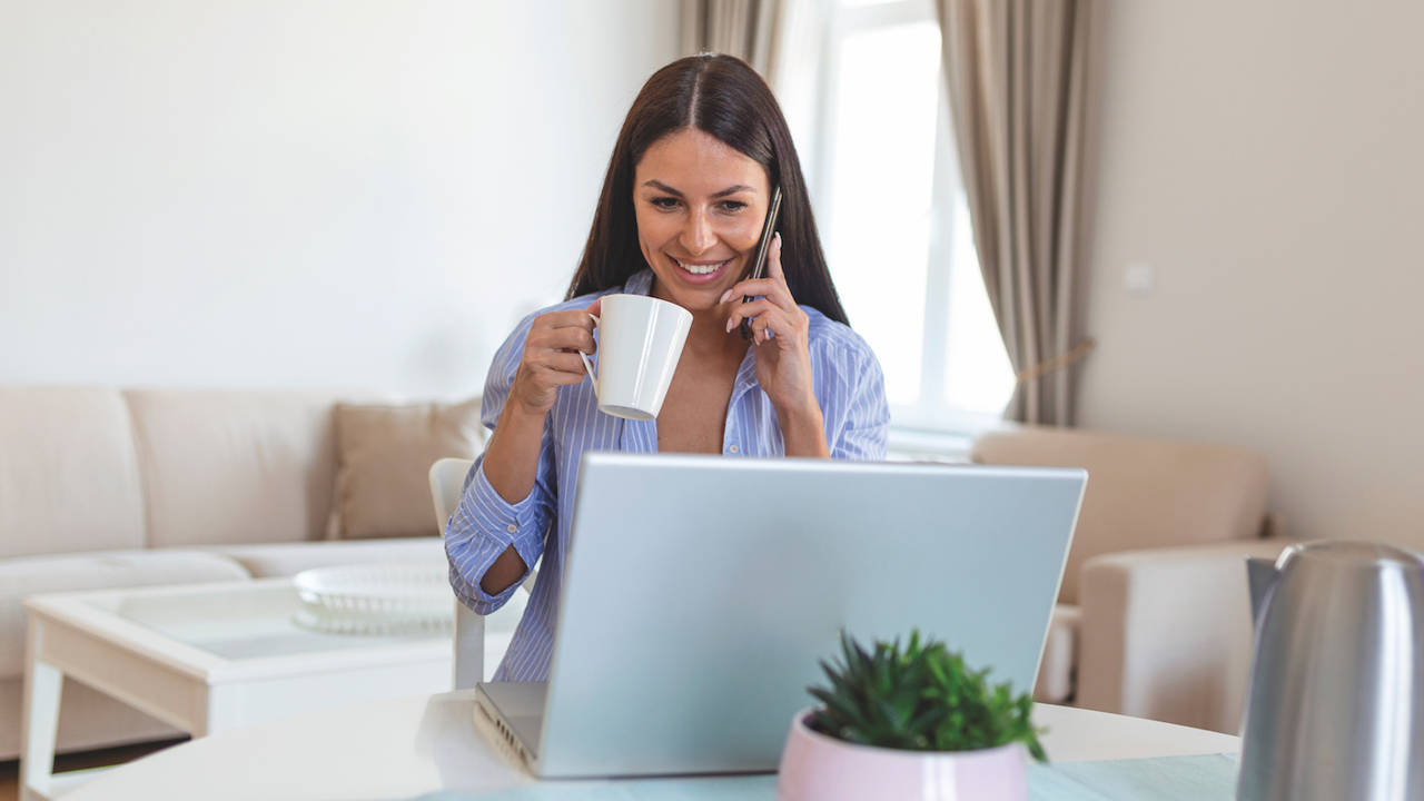self employed woman working with her phone laptop home with cup coffee happy woman using mobile phone while working home with laptop smiling woman messaging with smartphone