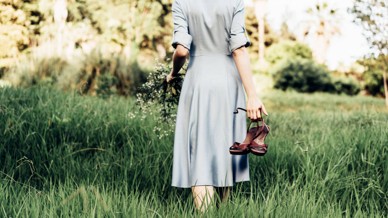 mujer descalza de espaldas caminando por la hierba