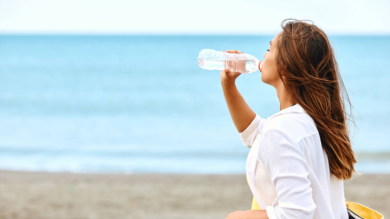 MUJER BEBIENDO AGUA EN LA PLAYA