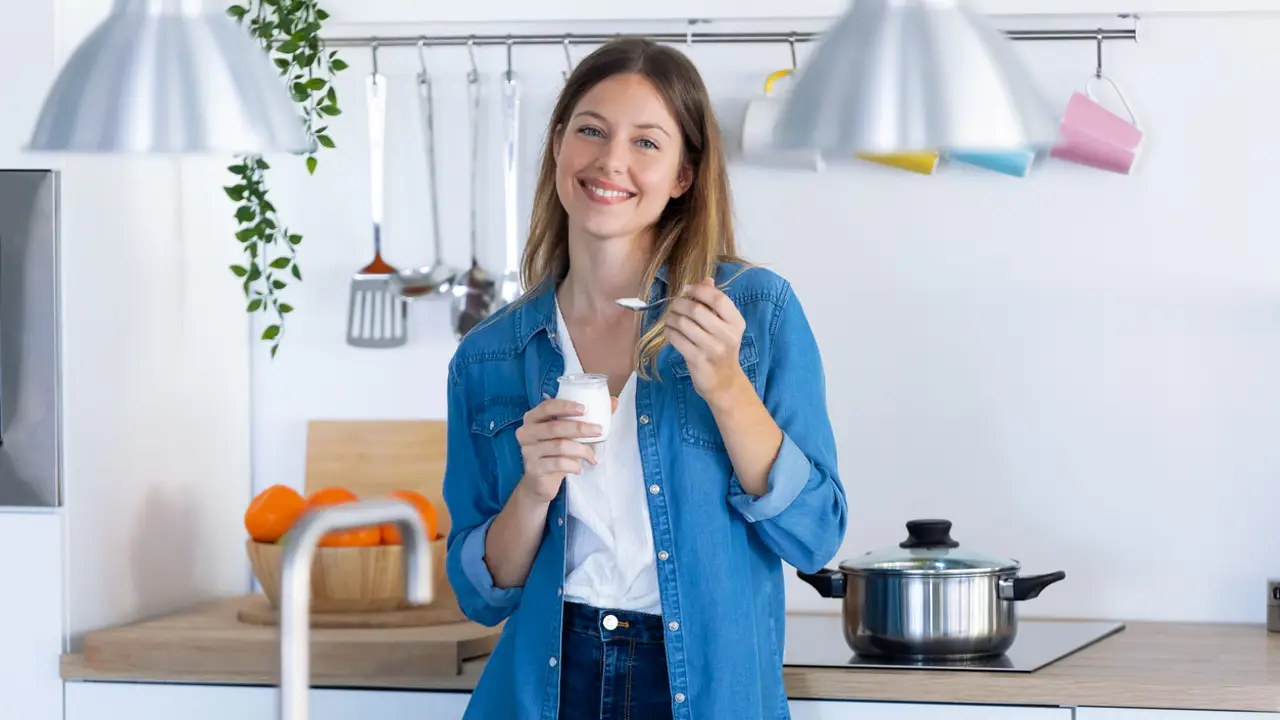 Mujer joven comiendo yogur en la cocina